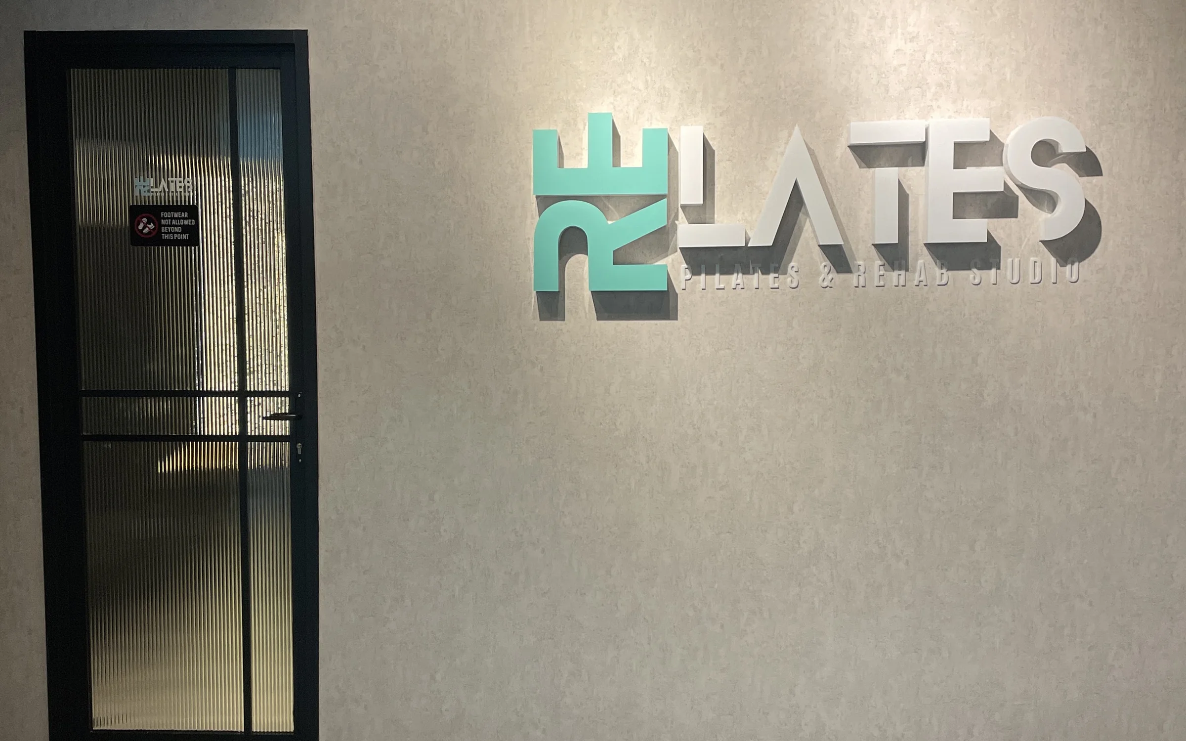The Re-Lates entrance: the teal and grey wordmark on a microcement wall
